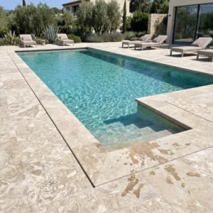 Cream travertine pavers with natural marbled veining surrounding a rectangular pool with sun steps, framed by olive trees and lavender in a Mediterranean-style backyard
