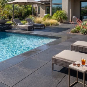 Dark charcoal stone paver pool deck and matching coping surrounding a clear swimming pool with woven lounge chairs.