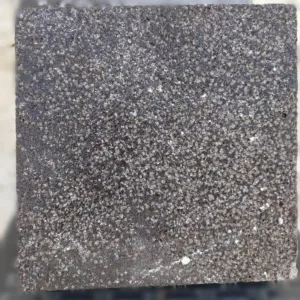 Textured bush-hammered black basalt cobblestones with a high-grip surface for safe outdoor paving in wet conditions.