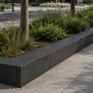 Dark charcoal curbstone forming a raised border between a landscaped planting bed and concrete walkway.