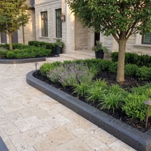 Smooth dark charcoal curved stone curbstones framing mulch garden beds with green shrubs along a light-colored paver walkway.