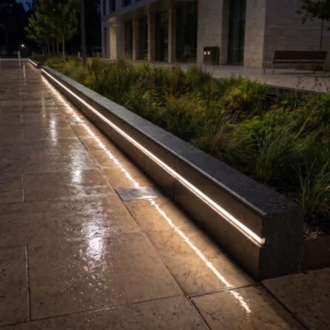 Dark charcoal curbstones with integrated warm LED strip lighting illuminating a wet paver walkway at night.