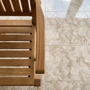 Vertical close-up taken from directly above, displaying the slatted wooden seat and armrest of a folding deck chair resting on glossy, highly reflective natural stone tiles featuring embedded fossilized shells.