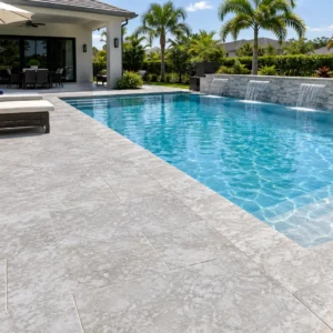 Silver-gray stone paving around a rectangular pool with three sheer spillways, wicker sunbeds and palm trees