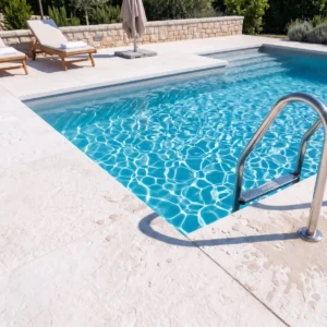Citadel Alabaster 36 white limestone pavers surrounding a pool corner with a stainless steel ladder, lounge chairs, and a stone garden wall
