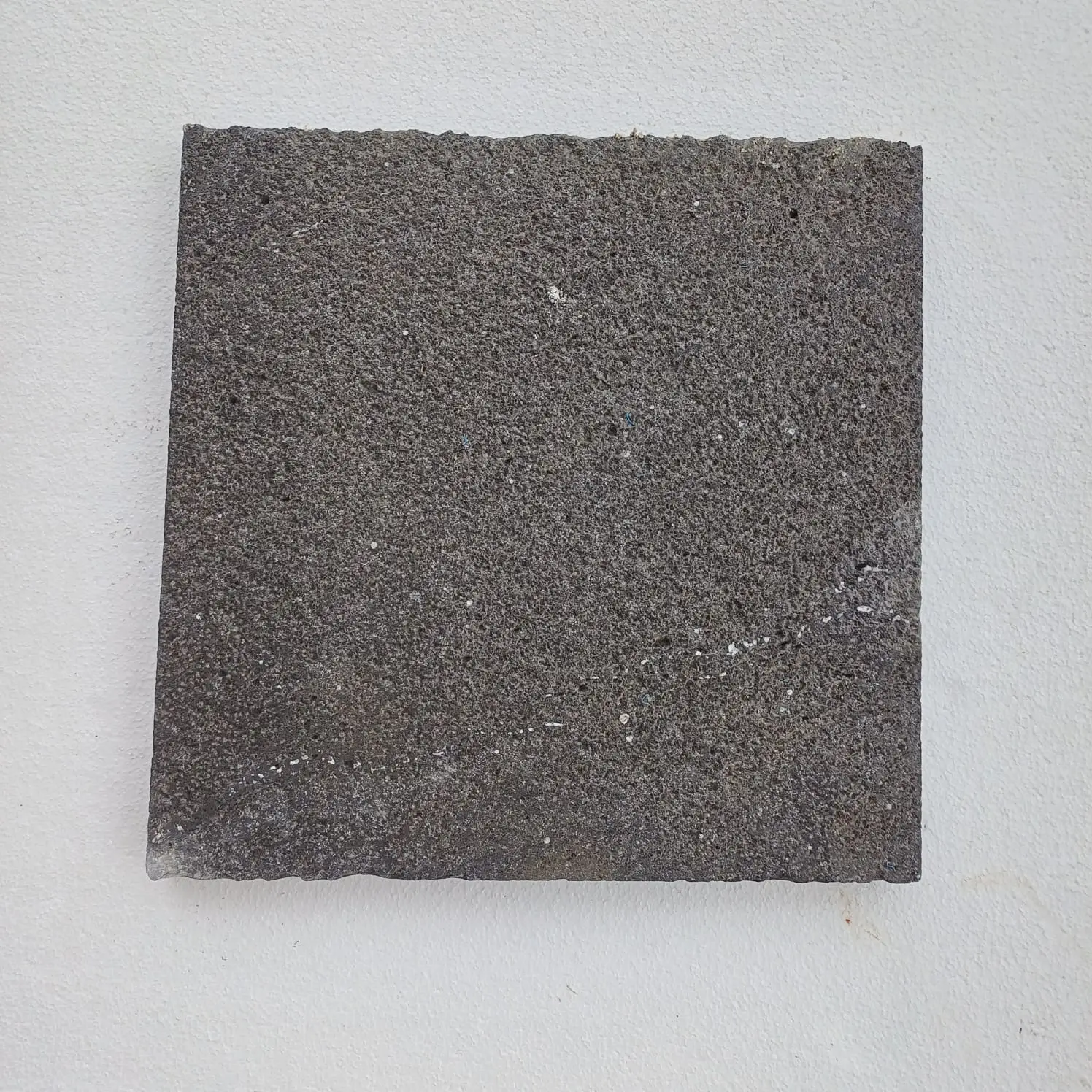 Dark Gray Textured Stone Slab Rough dark gray textured stone slab against a white wall.