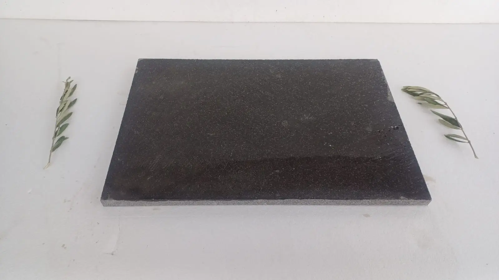 Dark Stone Slab with Olive Branches A dark, speckled stone slab is presented with two small olive branches.
