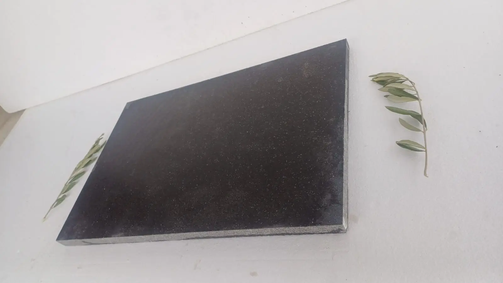 A dark stone slab is placed on a white surface with two olive branches.