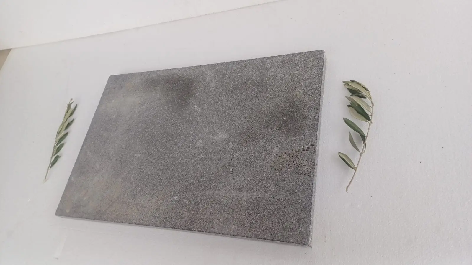 A textured gray stone slab is placed on a white surface with two olive branches.