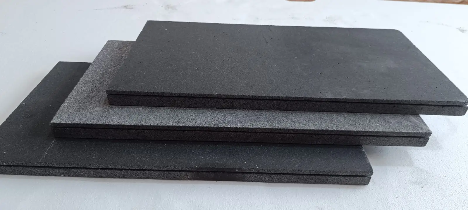 Several dark gray rectangular tiles stacked on a white surface.