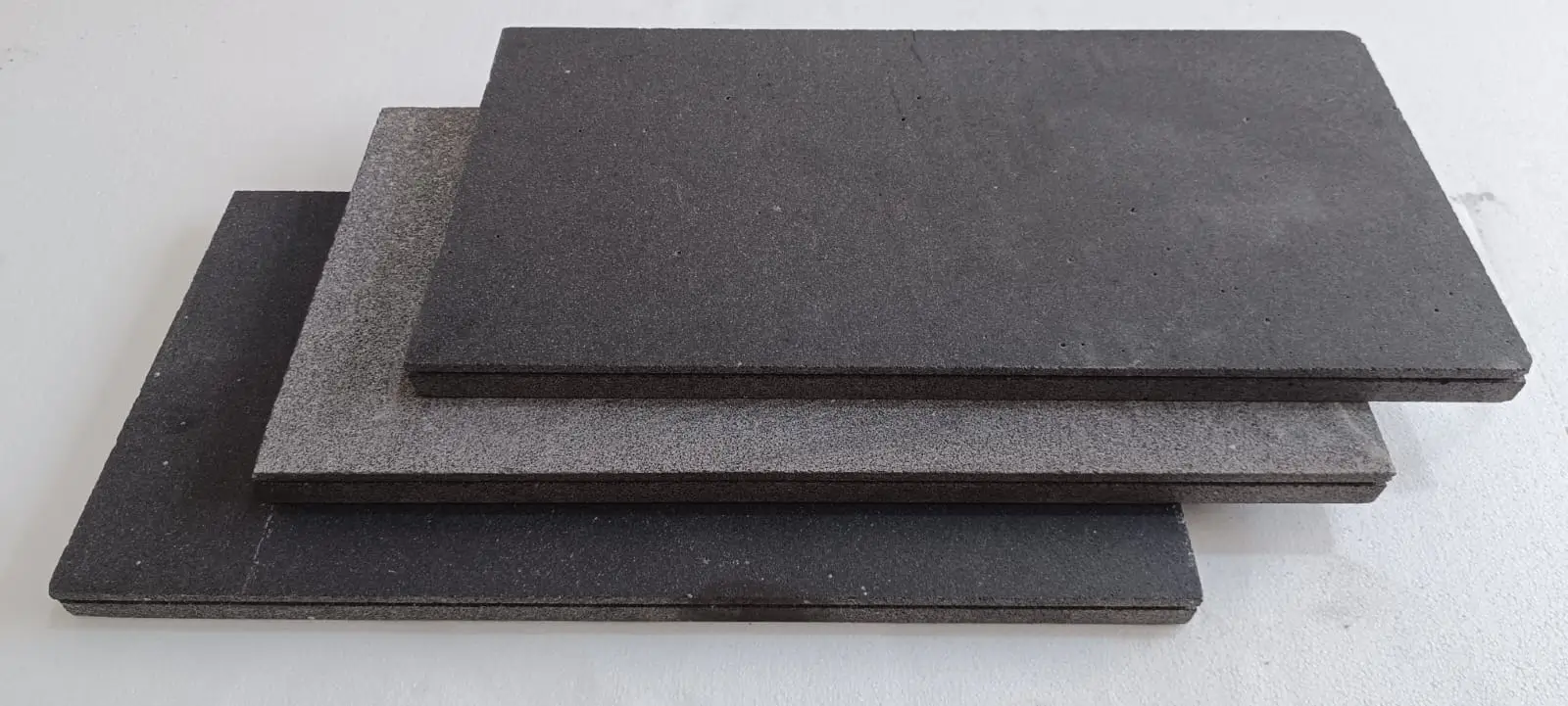 Three rectangular textured panels in shades of gray are neatly stacked on a white surface.