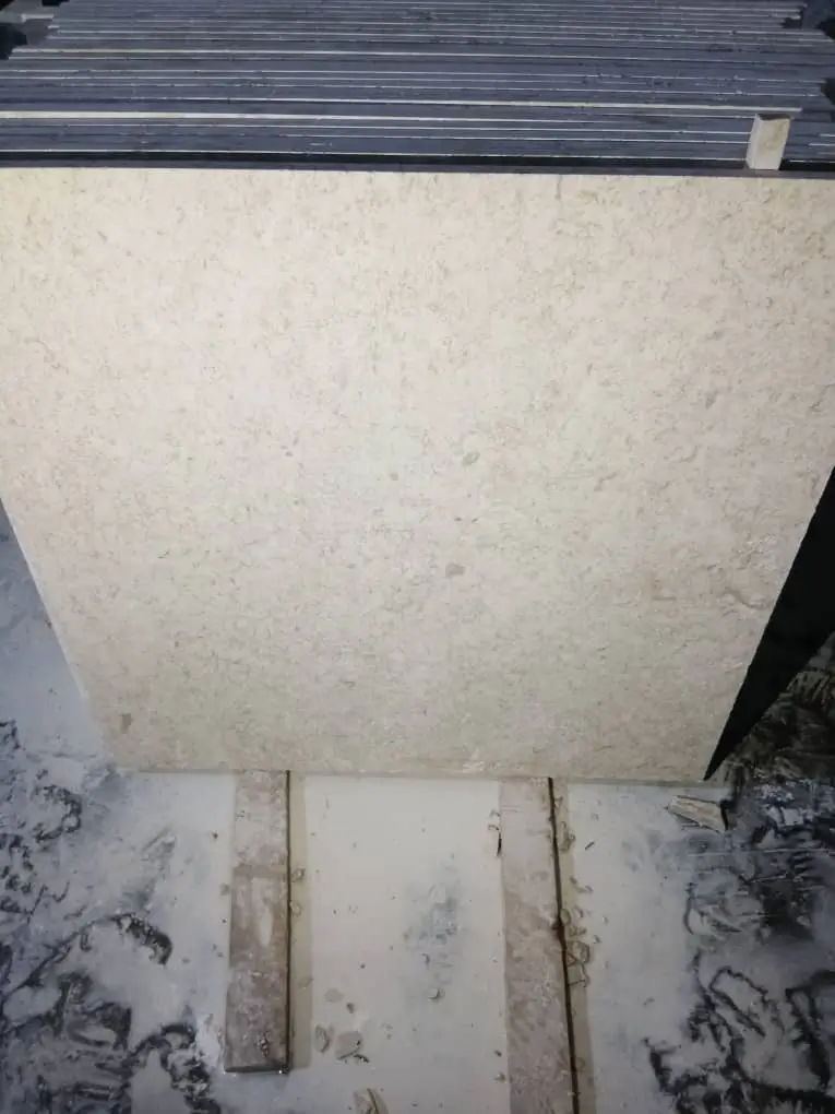 A beige limestone slab with natural texture is displayed in stacks.