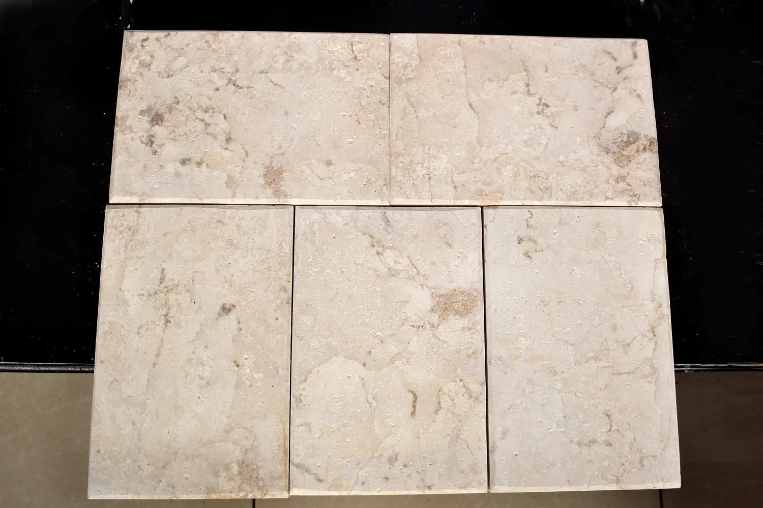 Top view of six beige travertine tiles with natural veining patterns.