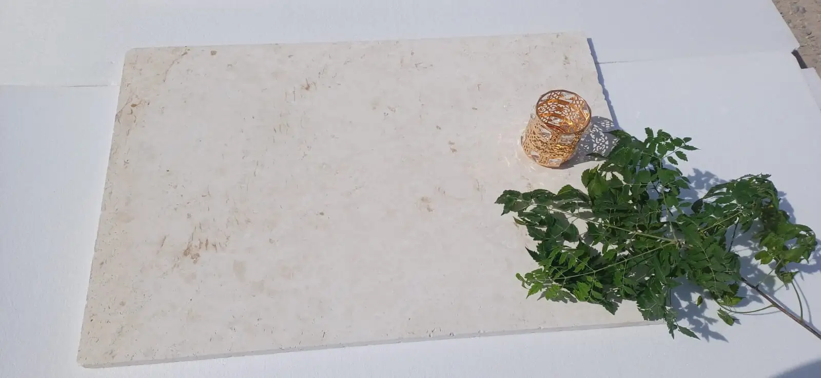 A light beige travertine slab with a decorative gold glass holder and green leaves.