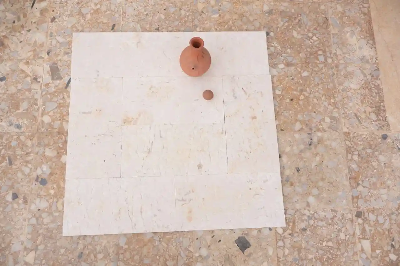 A small clay pot and a round ball rest on light-colored square tiles.