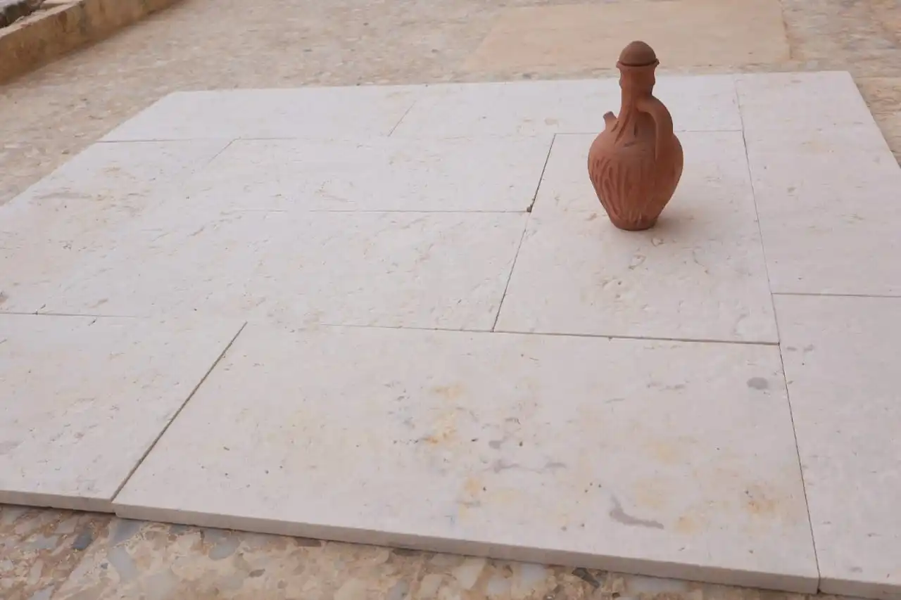 A rustic clay jug with a handle sits on a light-colored stone tiled surface.