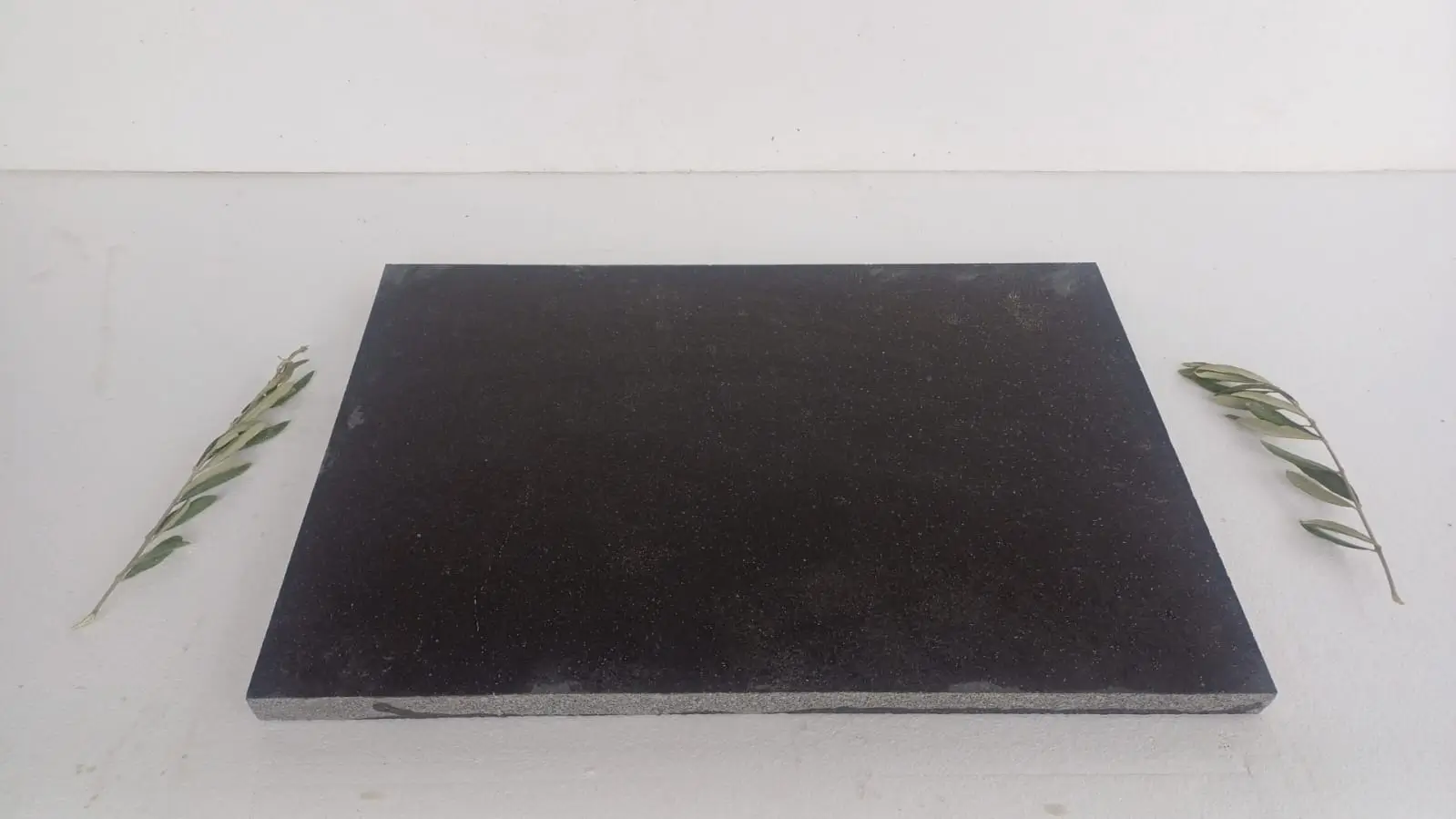 Dark speckled granite slab on white surface with olive branches.