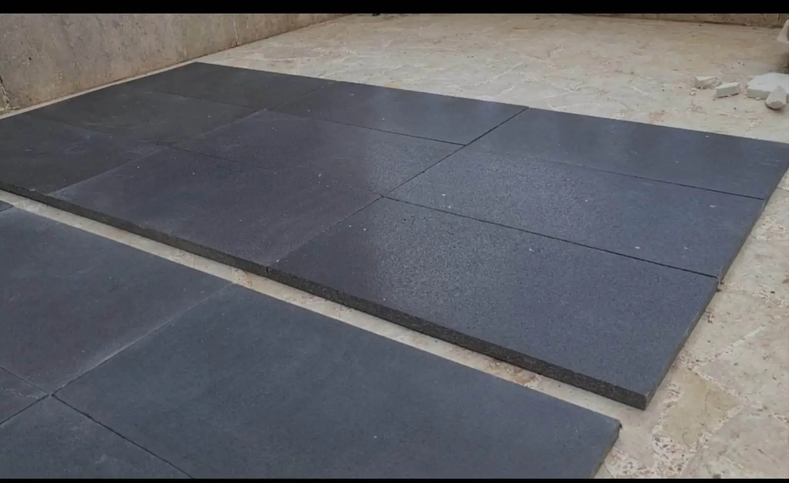 Several dark gray interlocking rubber mats laid out on a concrete floor.