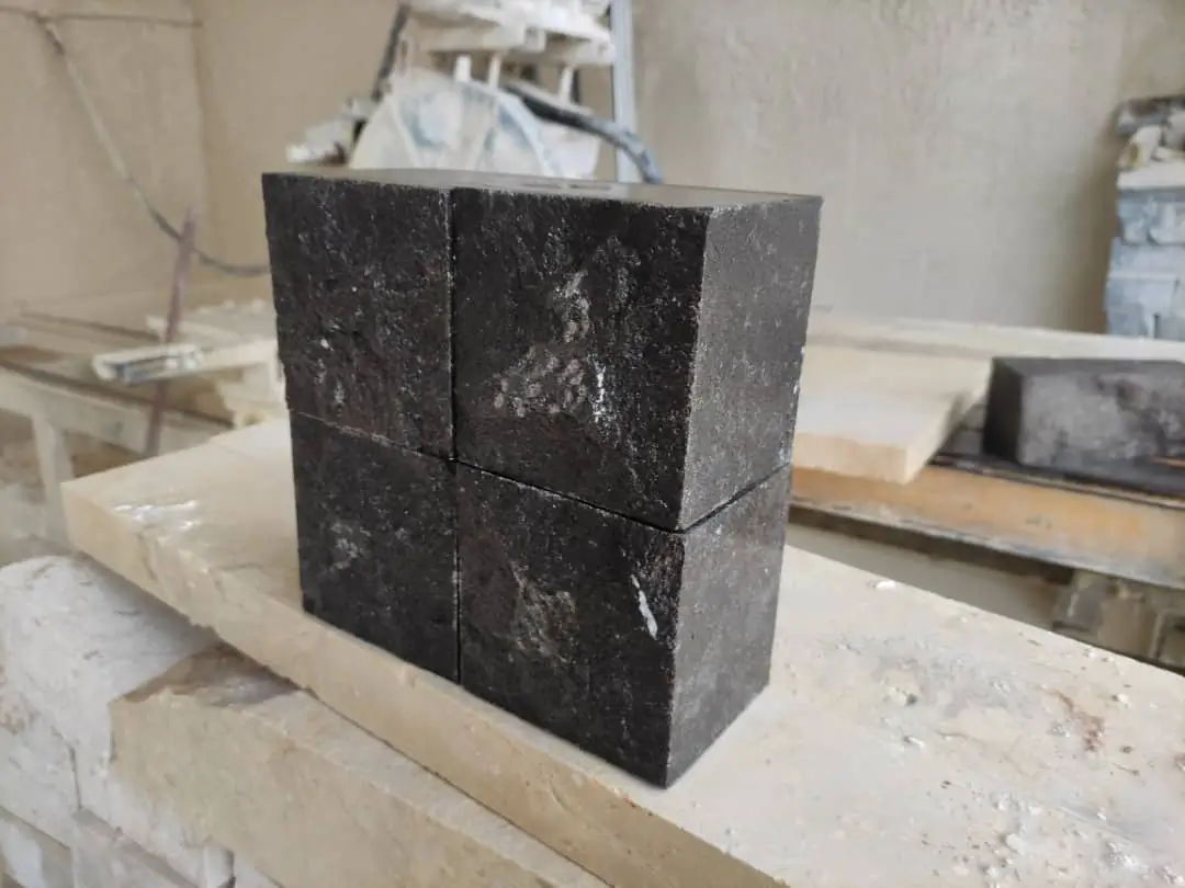 Four dark, rough-textured stone blocks stacked together on a wooden surface.