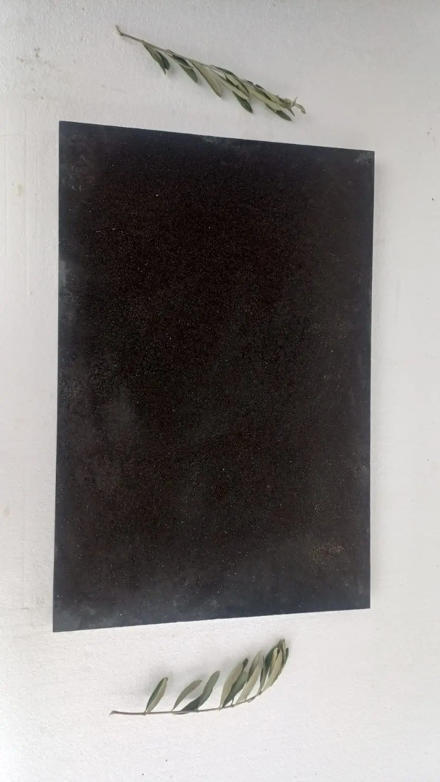A dark rectangular stone slab rests on a white surface with olive branches.