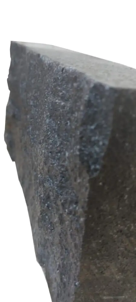 A close-up of a dark, speckled, textured stone surface with rough edges.