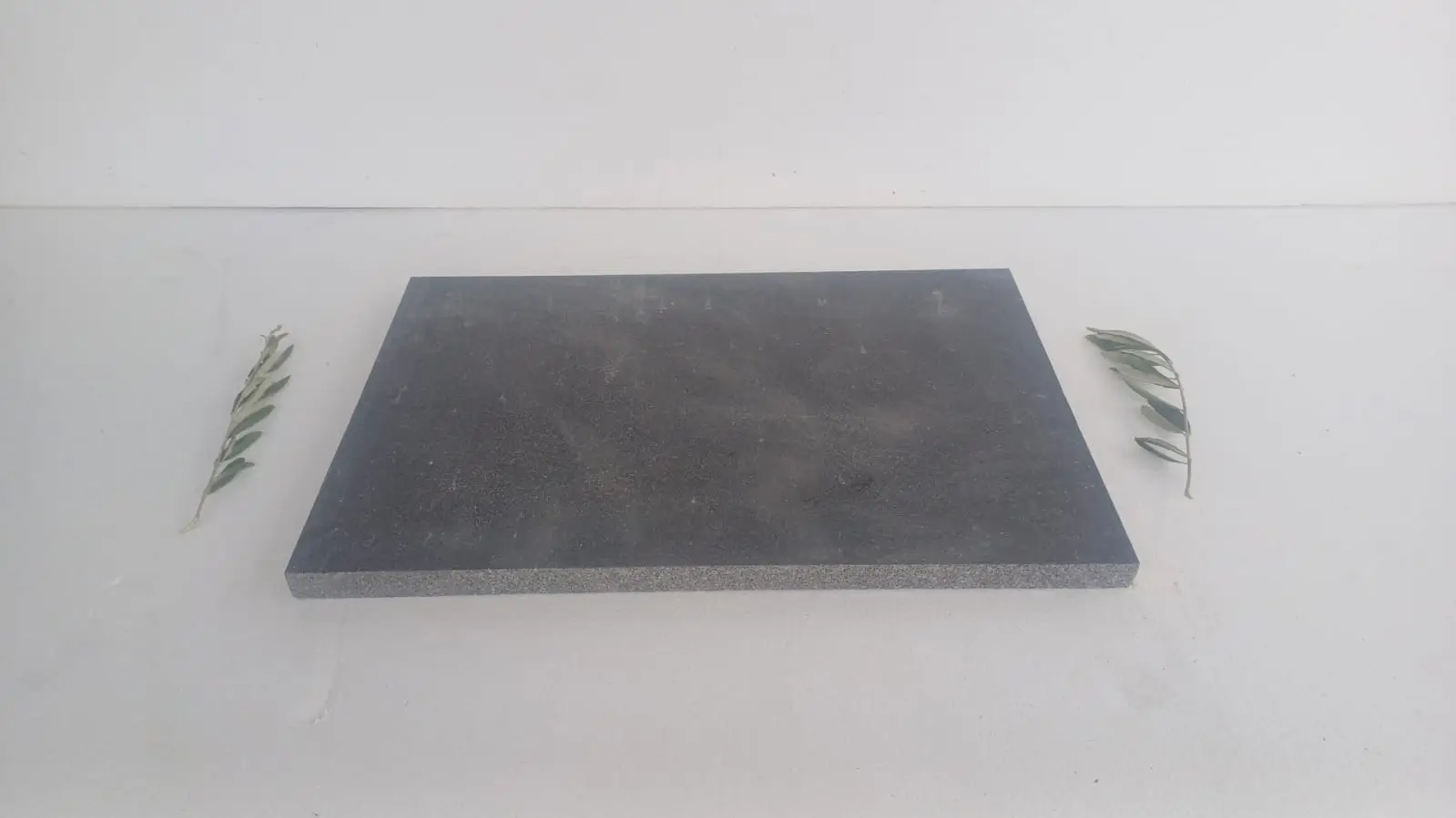 A dark, rectangular stone slab is centered on a white surface with olive branches on either side.