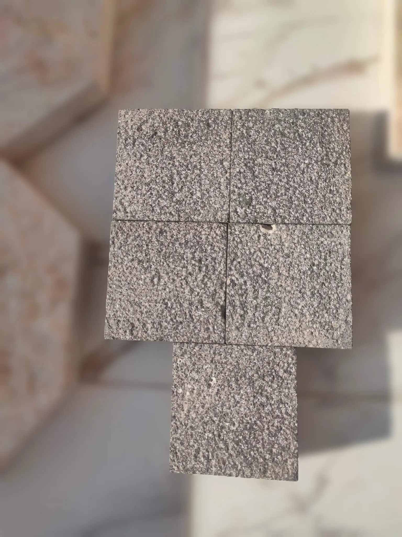 A stack of square granite pavers with a speckled textured surface.
