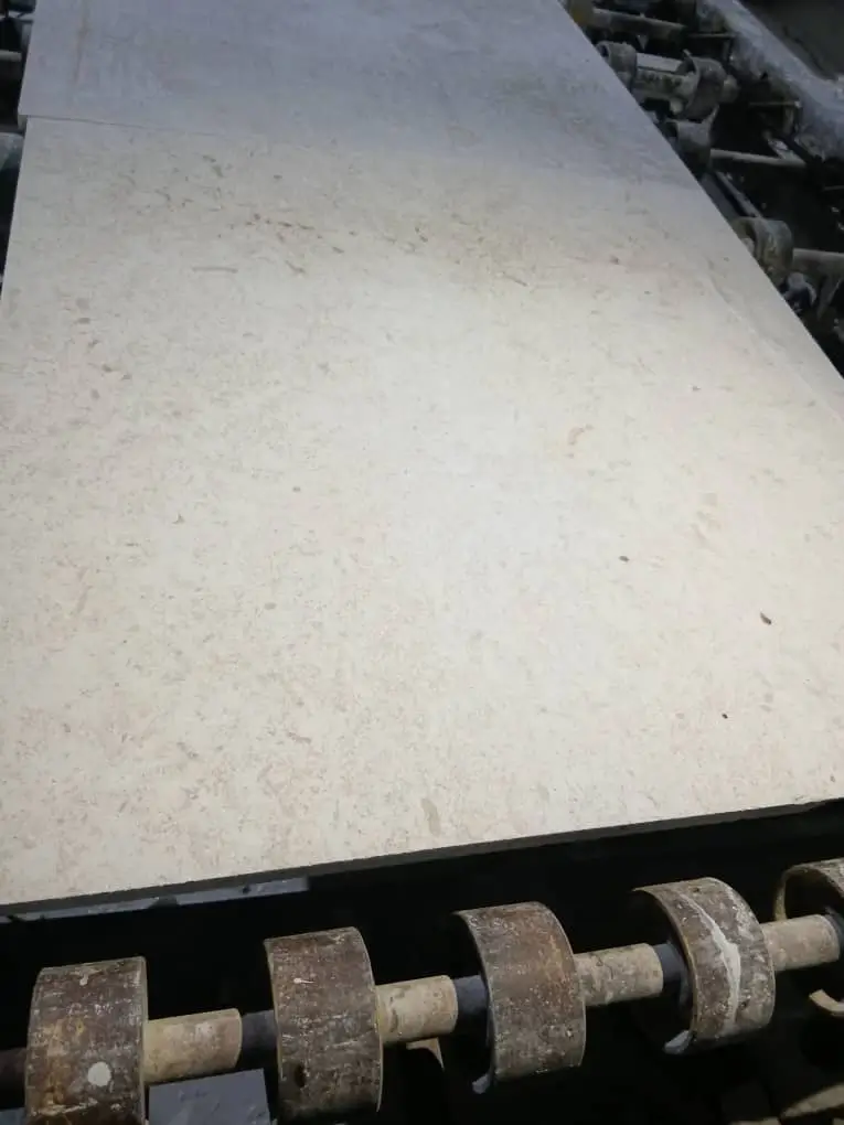 Close-up of large, light beige stone slabs with subtle speckling on a conveyor.
