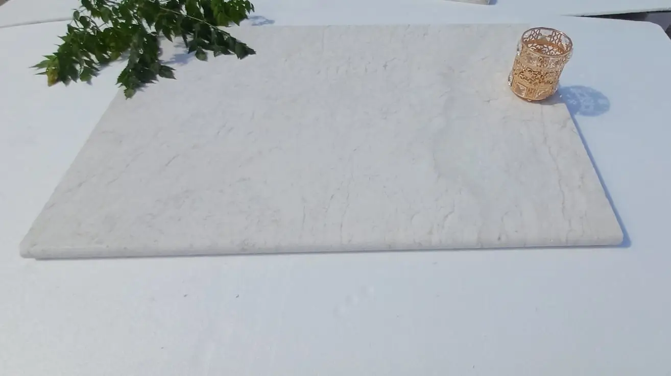 Light Marble Slab with Greenery Accent A light-colored, veined stone slab with a decorative golden holder and green leaves.