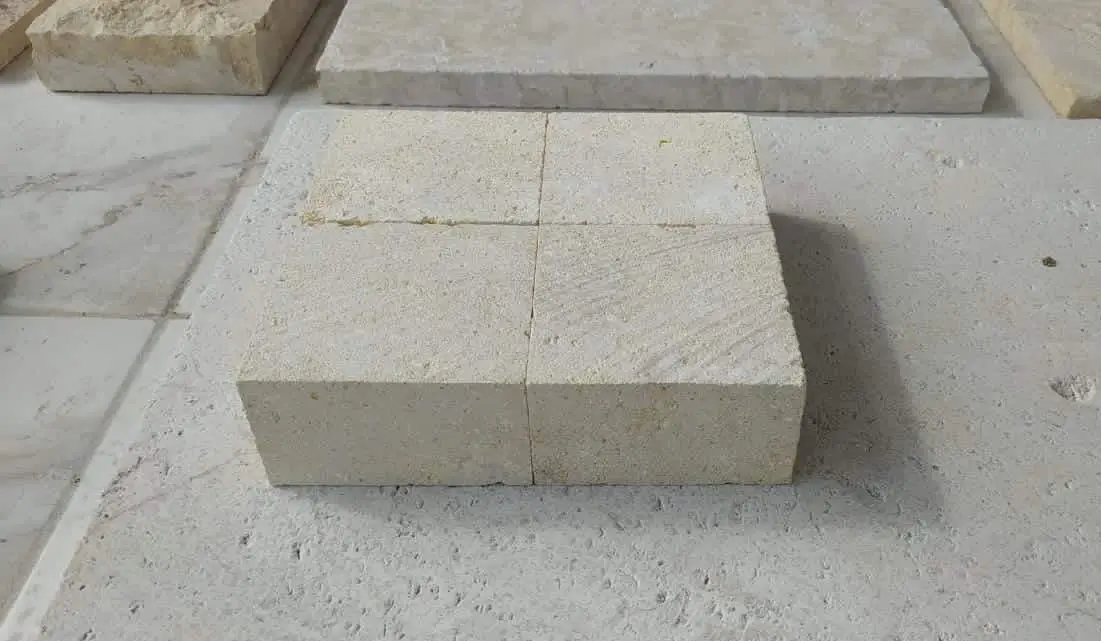 Four light tan stone blocks arranged in a square formation on a textured surface.