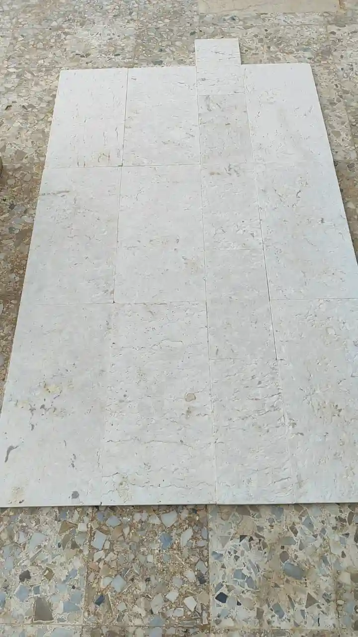 A collection of light gray natural stone tiles laid out on a textured floor.