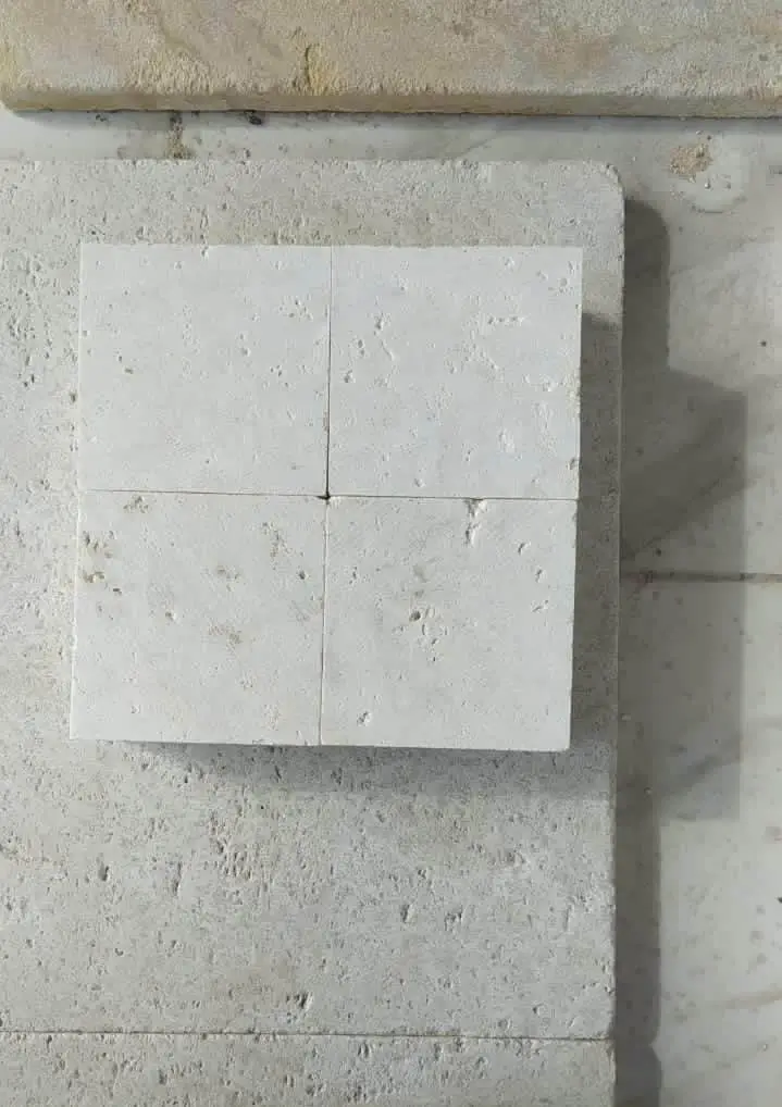 Four square textured limestone tiles are arranged on a larger stone surface.