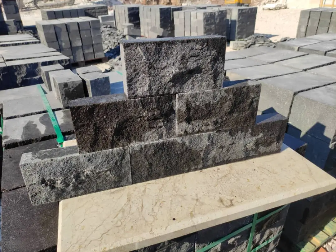 Stacked dark grey granite blocks with rough textured surfaces outdoors.