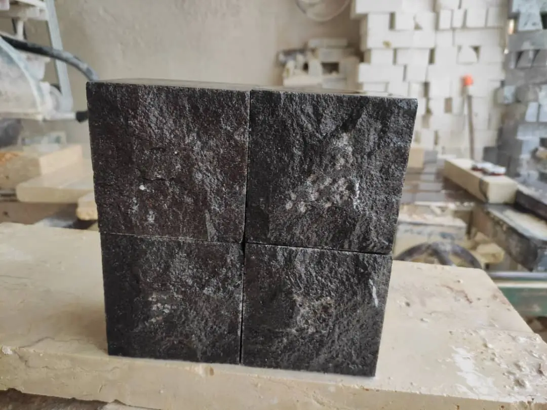 Stacked Dark Stone Blocks Four dark, textured stone blocks are stacked together in a cube formation.