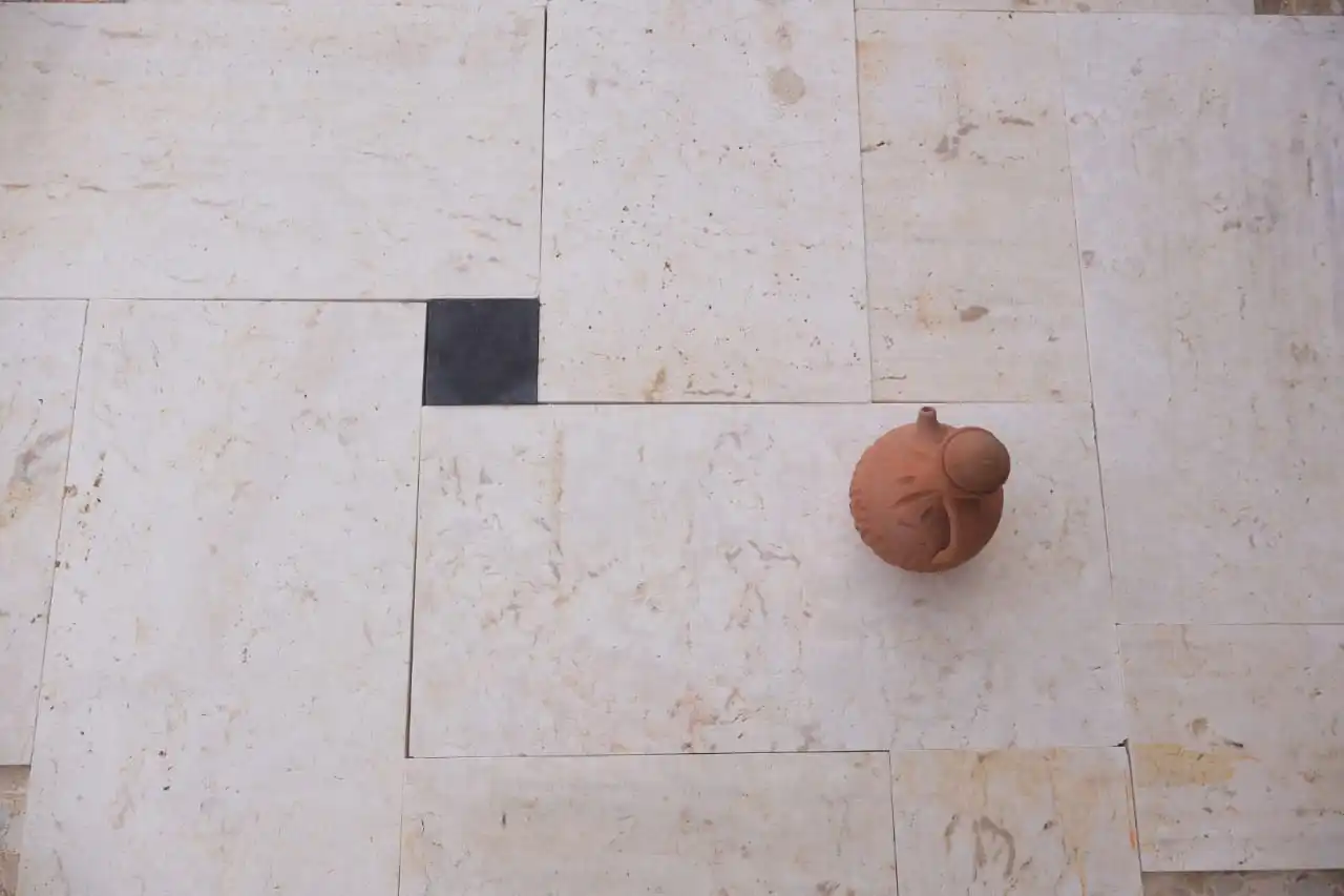 A small terra cotta jug sits on a light-colored stone tile floor.