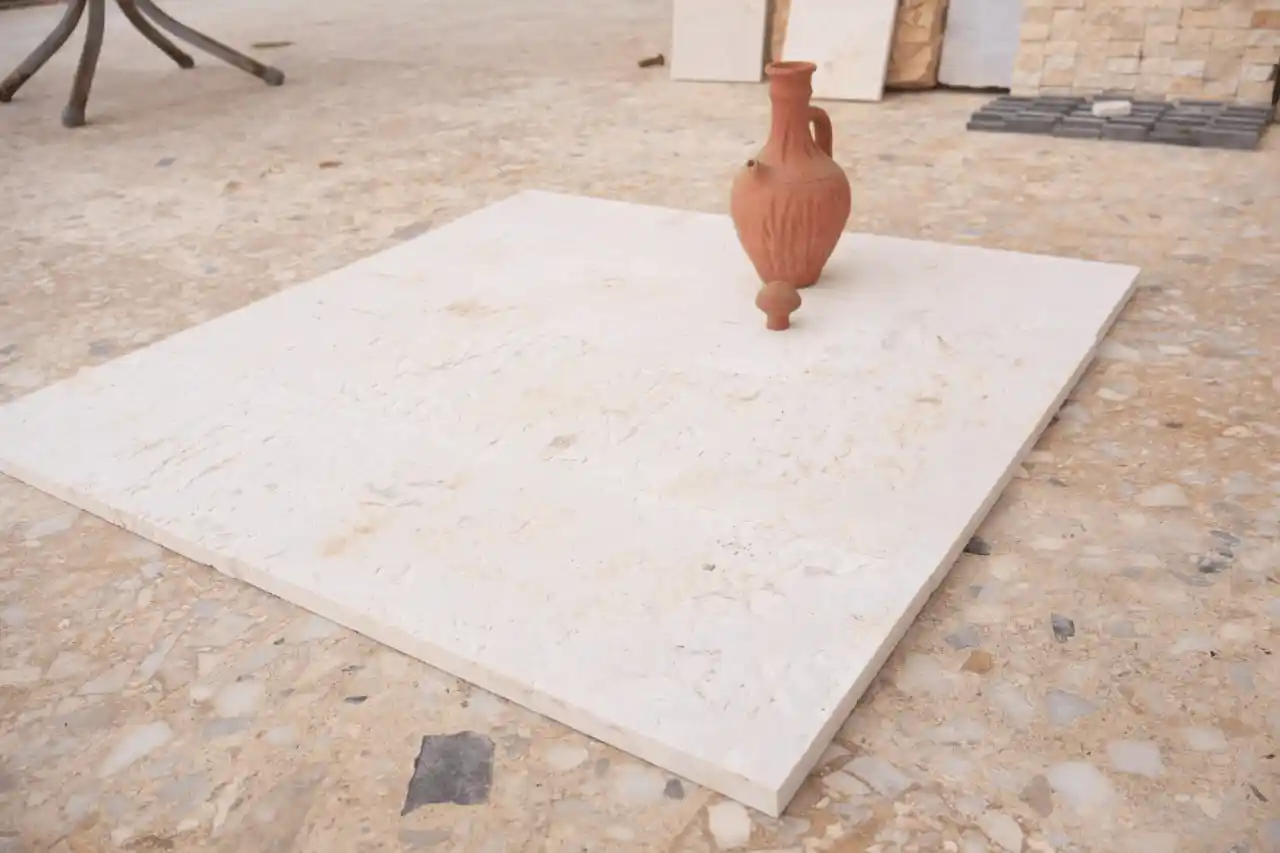 An antique terracotta pitcher sits on a cream-colored stone tile.
