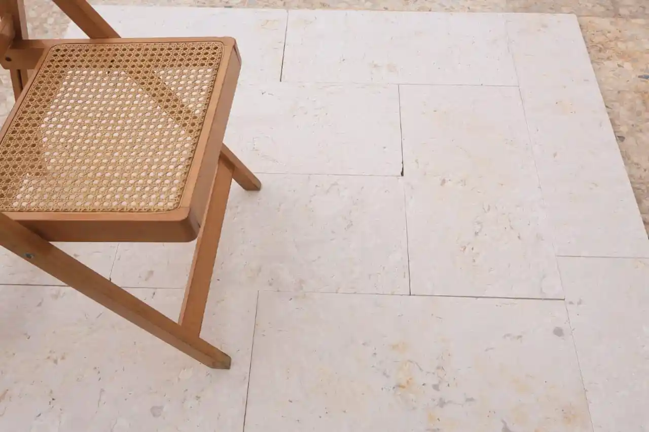 A wooden chair with a woven seat rests on light-colored, textured stone patio pavers.