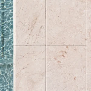Direct overhead top-down view of a swimming pool edge paved with smooth Royal Cream limestone pavers, showing light cream colors and subtle veining right next to clear blue water.
