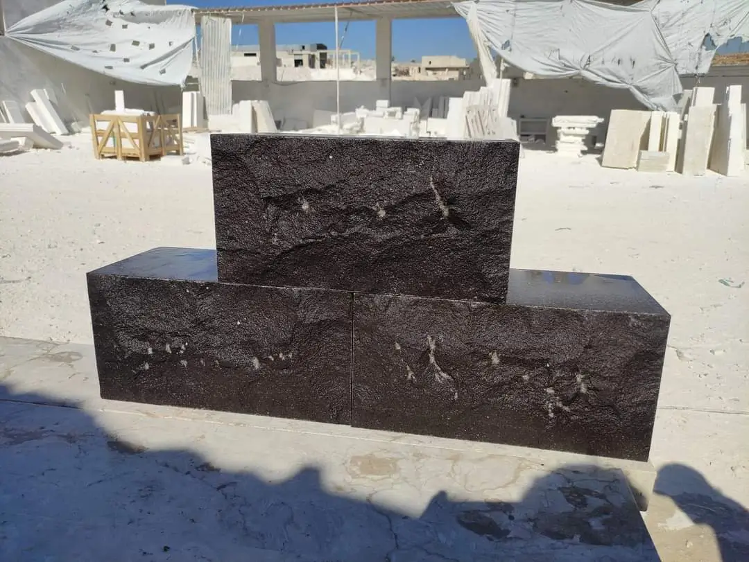 Two dark textured stone blocks sit in front of another dark stone block.