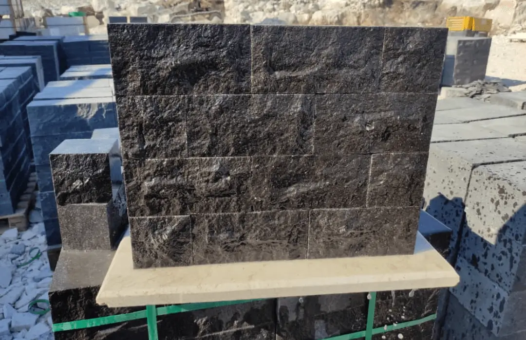 Stacked dark stone wall cladding with rough texture displayed outdoors.