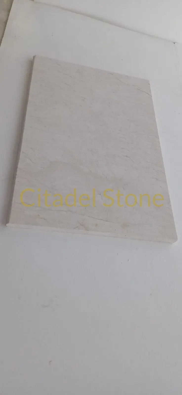 A light-colored marble tile with subtle veining, displayed on a flat surface, a natural stone garden wall example worth examining.
