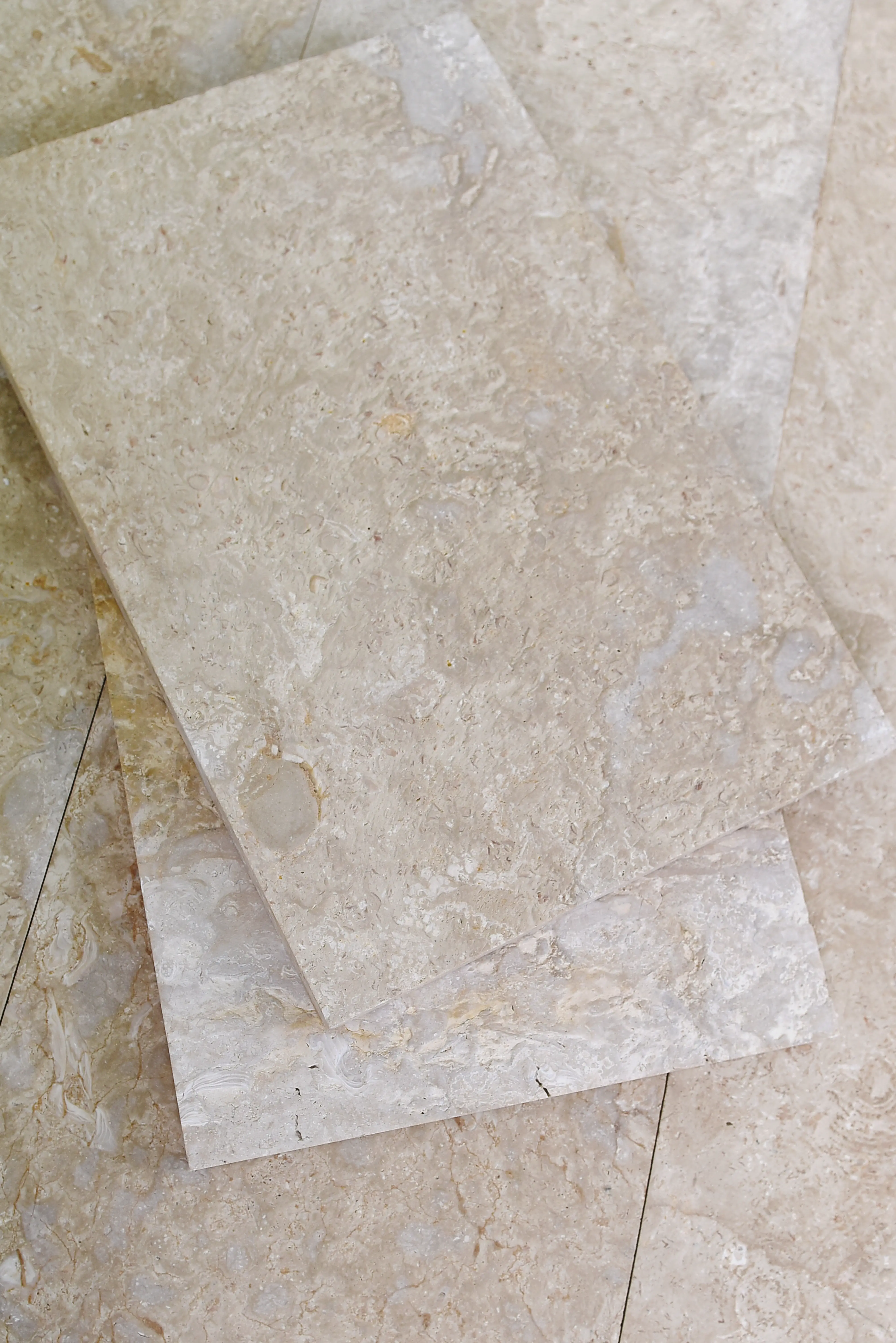 Close-up view of stacked beige travertine tiles showing natural veining and texture, shown for flagstone vs bluestone paving.