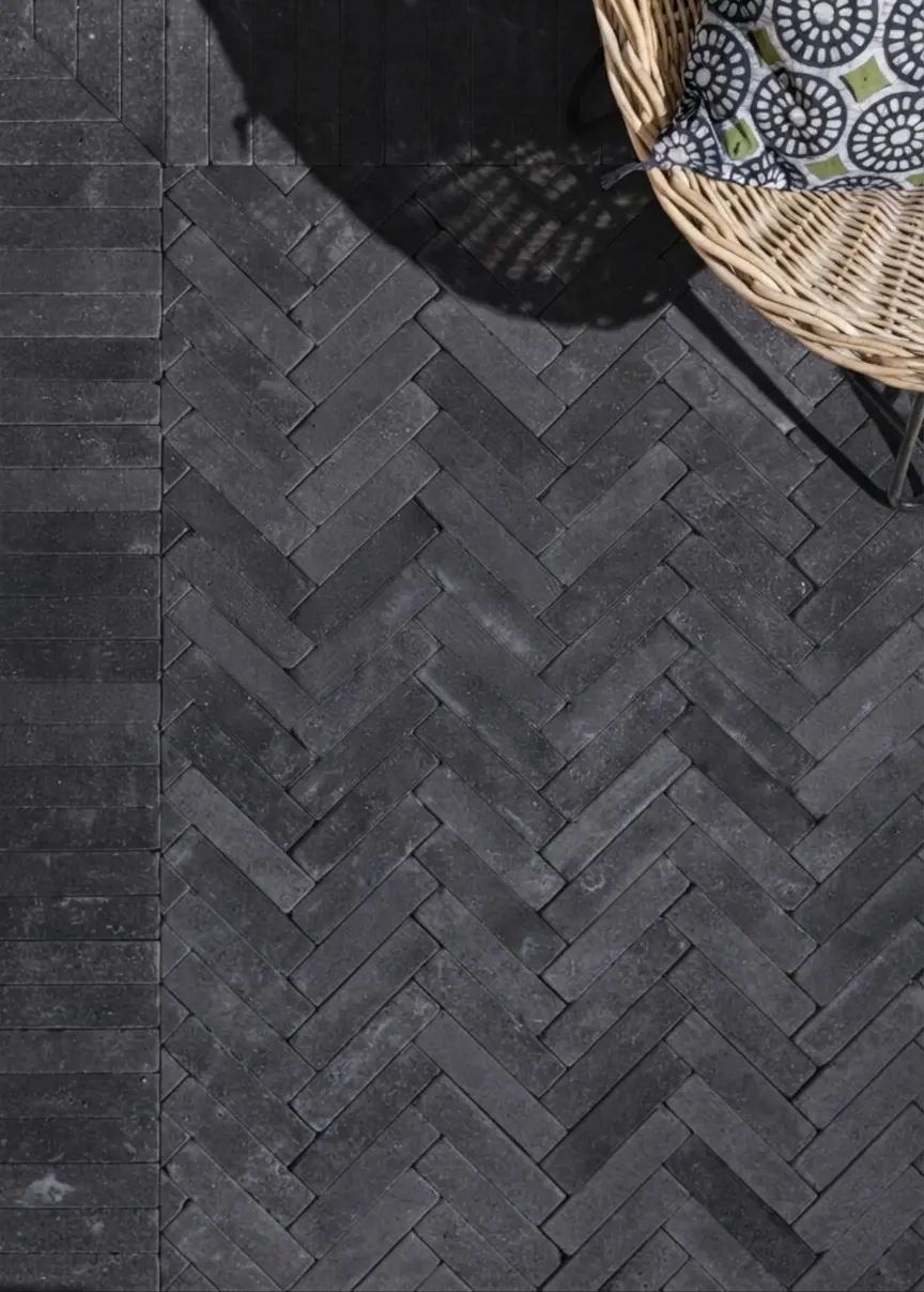 Dark basalt pavers laid in a precise herringbone pattern for outdoor flooring, an example for cobblestone setts vs clay pavers.