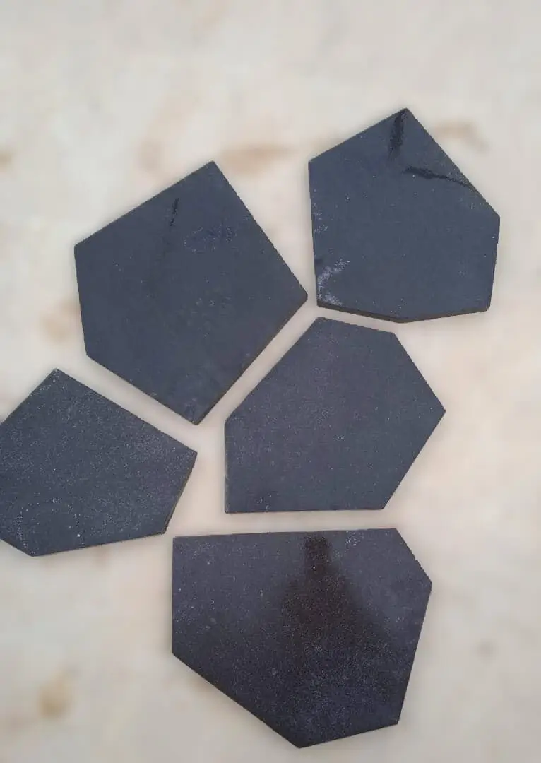 Dark Hexagonal Stone Pieces Scattered Several dark hexagonal basalt tiles scattered on a light marble surface, relevant to travertine falls.