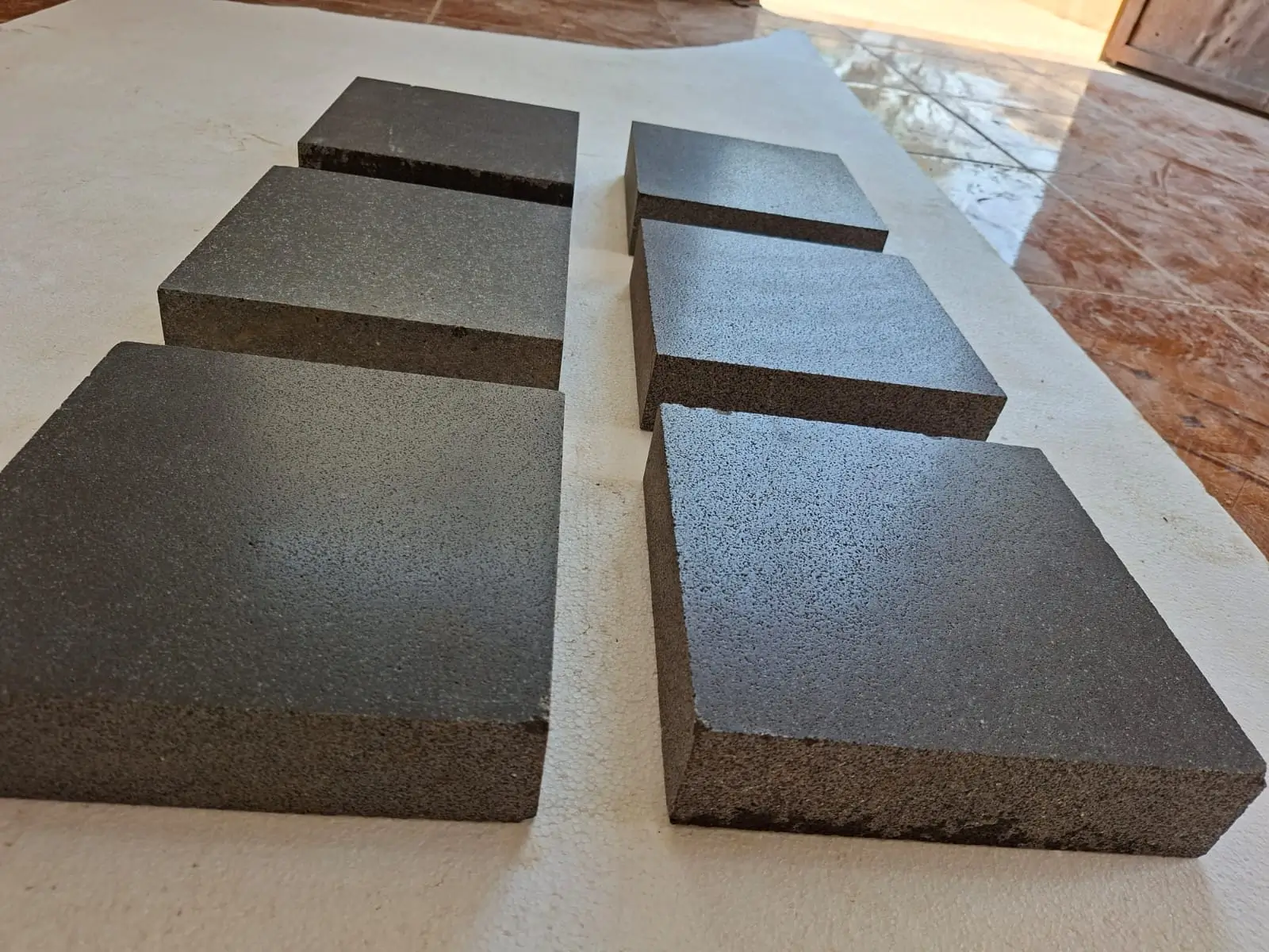 Dark Square Stone Pavers Several dark gray basalt pavers are neatly arranged on a textured white surface, showcasing their texture, an example for cobblestone sett settling problems.