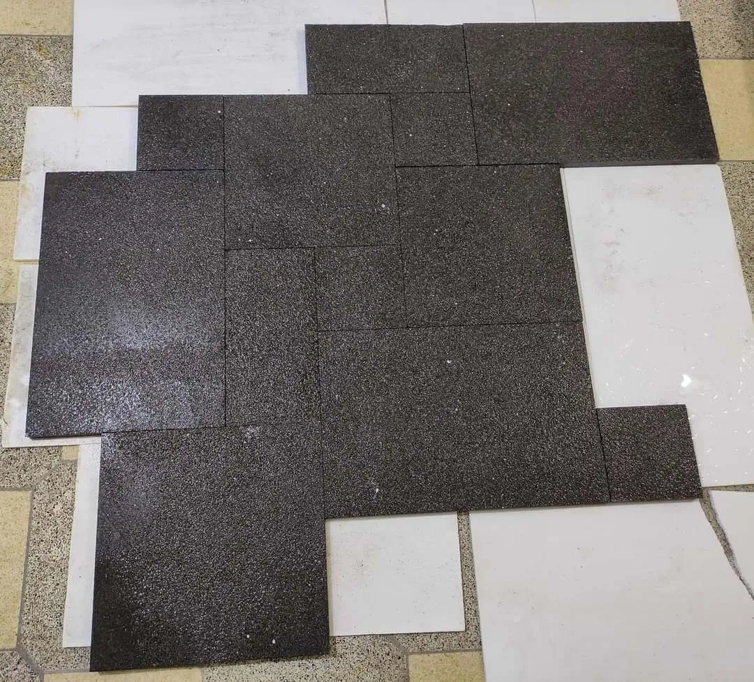 Dark granite pavers arranged with white tile slabs on a textured surface, a reference for ivory travertine sealing problems.
