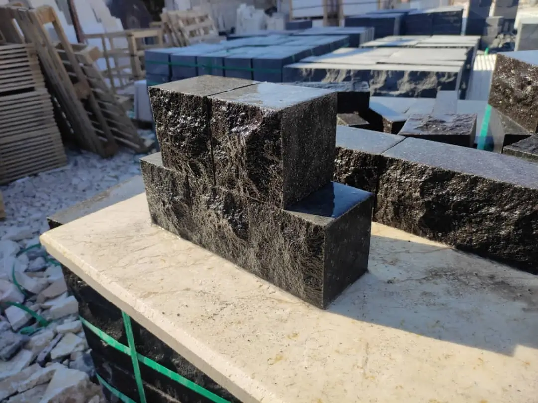 Rough textured dark cobblestone pavers stacked neatly on a light stone surface, relevant to Limestone Cobblestone Pavers.