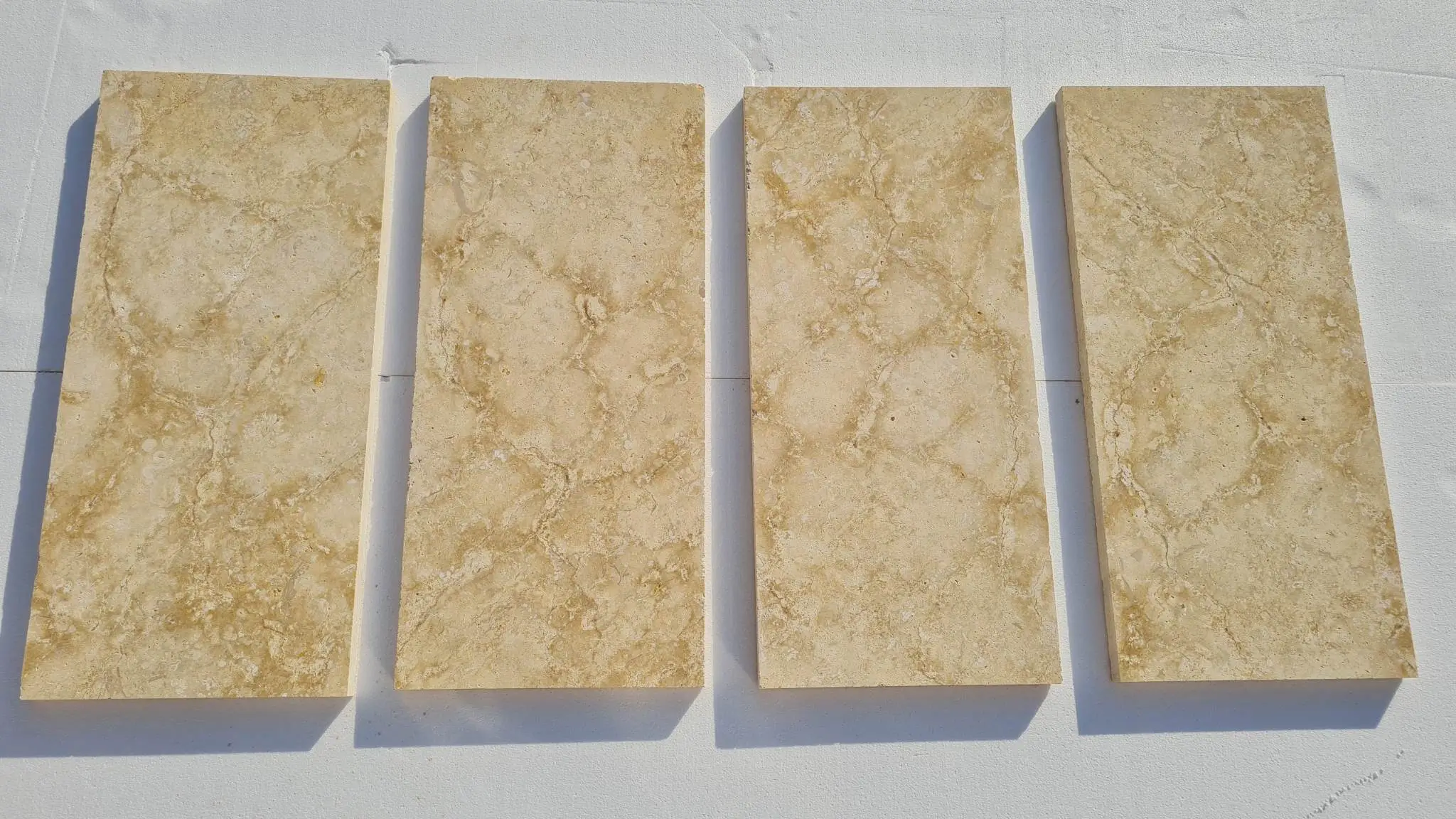 Four rectangular beige marble tiles display intricate veining patterns on a white surface, an example for scabos travertine pool coping.