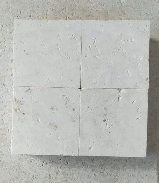 Four square white travertine tiles with subtle pitting arranged on a concrete surface, pictured for granite cobblestone.