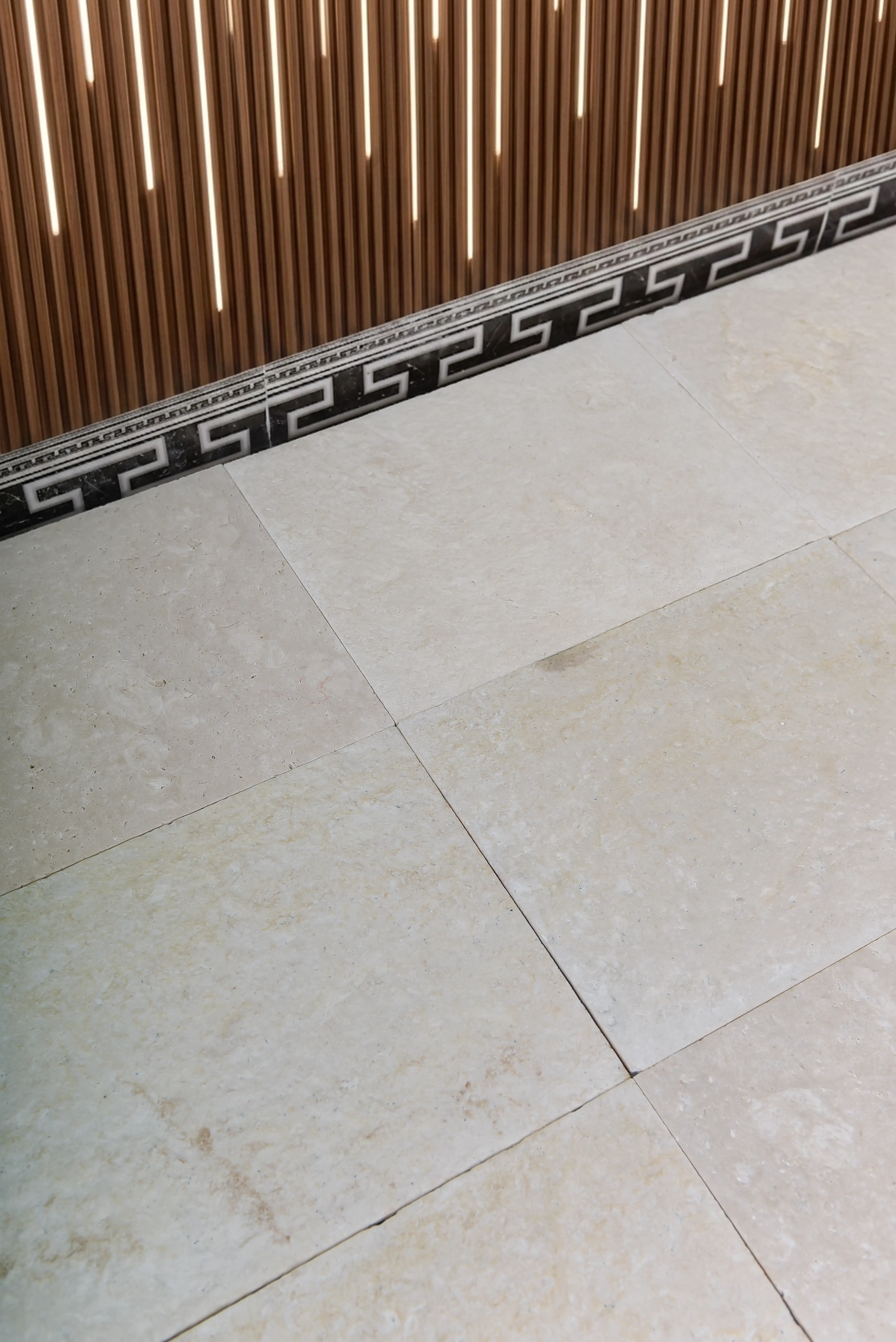 Beige limestone floor tiles with a decorative Greek key border pattern, an example for white pool tile options.
